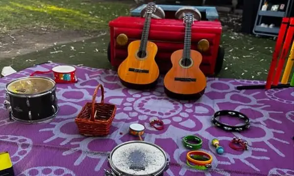 Outdoor music circle on a picnic rug: small guitars, hand drum, tambourines and percussion instruments from Reverse Garbage.