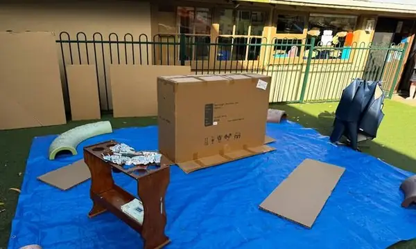 Open-ended outdoor painting set-up: large cardboard boxes as canvases on a tarp for whole-body mark-making.