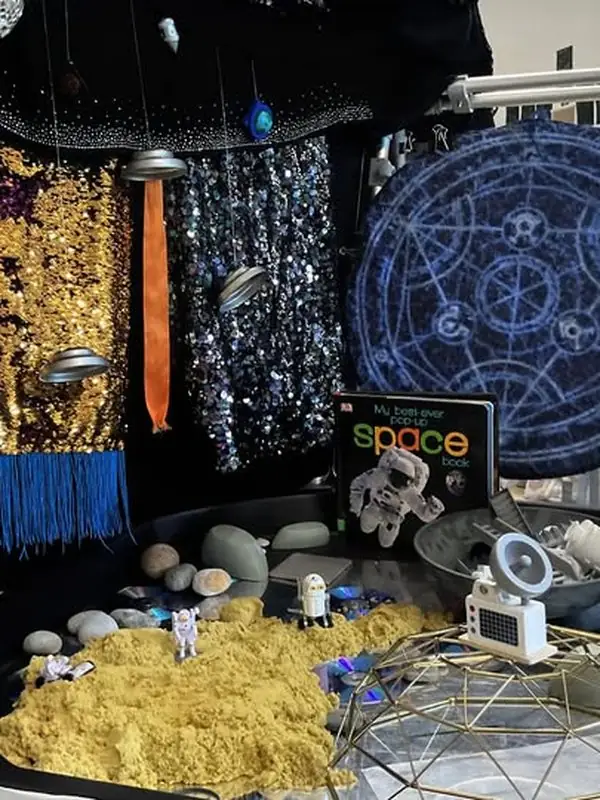 World Space Week play: sequin galaxies, starry backdrop, pop-up space book, and a sand tray with astronauts and craters.